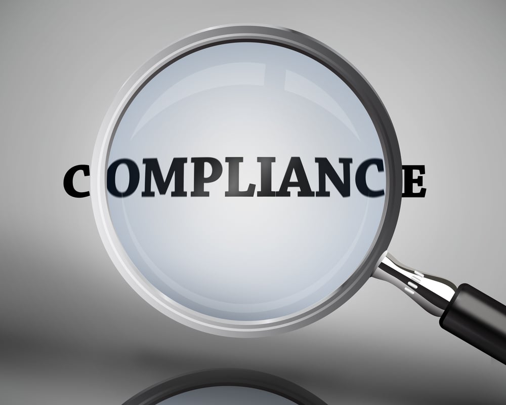 Magnifying glass showing compliance word on grey background Magnifying glass showing compliance word on grey background